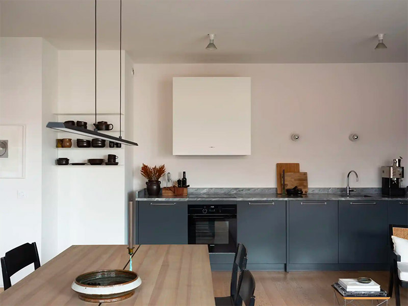 In deze stoere keuken, met grijsblauwe kasten en marmeren werkblad, is er gekozen voor een strakke witte ombouw voor de afzuigkap.