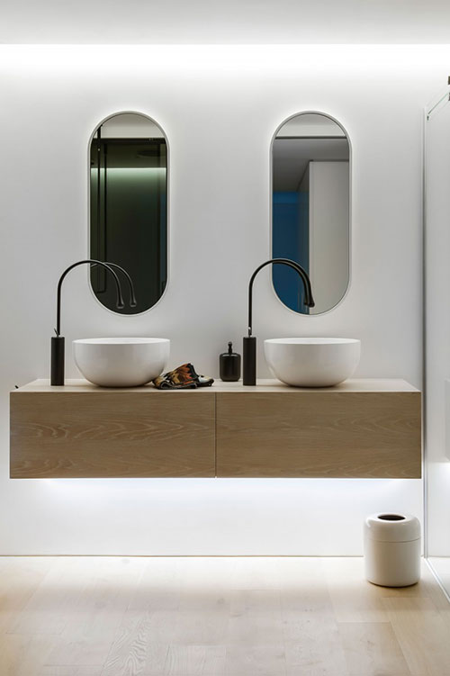 Ovale spiegels boven witte waskommen op zwevende houten badmeubel