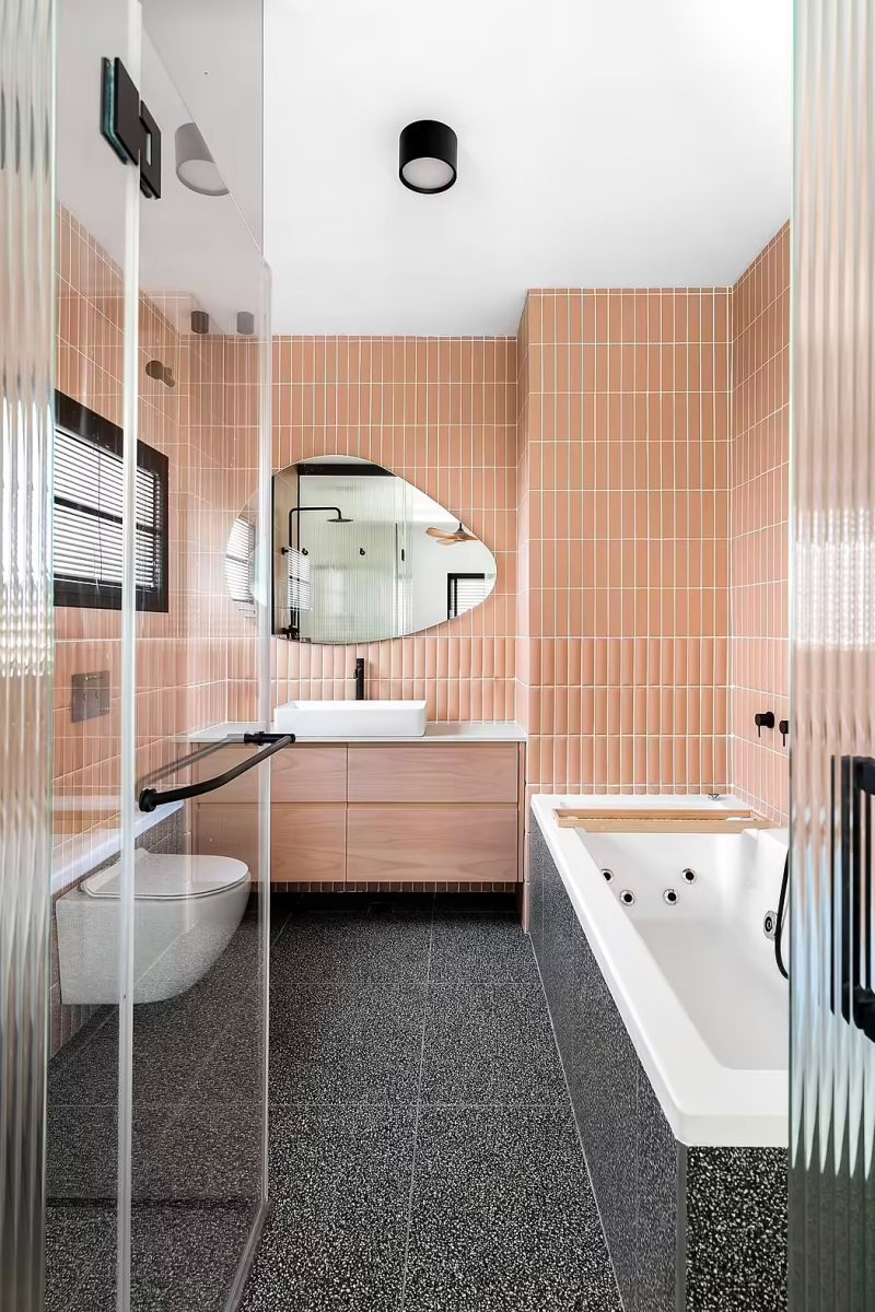 Studio Gal Gerber heeft deze mooie badkamer ontworpen, gekenmerkt door roze wandegels, gecombineerd met zwarte tegels en een warme houten badkamermeubel. 