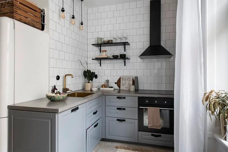 Een super leuke l-vormige keuken met blauw-grijze keukenkasten, betonnen keukenblad en witte keuken achterwand tegels.