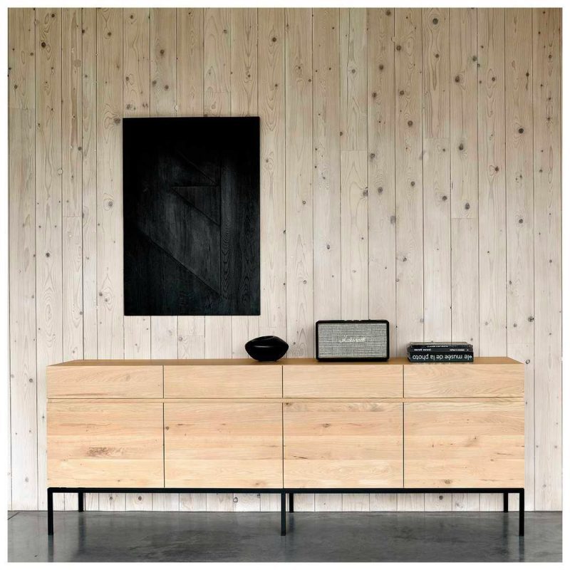 In deze woonkamer is de Ethnicraft Ligna Black dressoir tegen een houten wand geplaatst. Het Ligna Black Dressoir van Ethnicraft is gecreëerd door Alain van Havre. Dit prachtige designstuk bestaat uit massief eikenhout in het bovenste gedeelte, terwijl het onderstel is vervaardigd van zwart metaal. Het contrast tussen het warme eikenhout en het stoere zwarte metaal zorgt voor een unieke uitstraling. Hier verkrijgbaar voor € 2.919. 