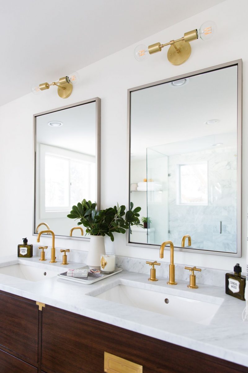 Dubbele wastafels met gouden kranen en wandlampen