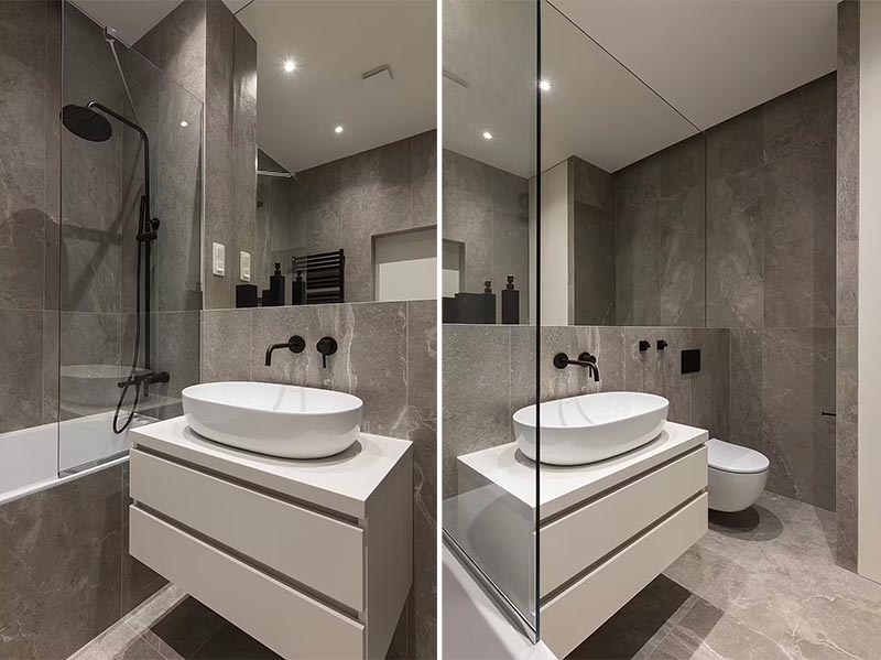 Deze moderne kleine badkamer is super strak en praktisch ingericht, met een bad en douche, een badkamermeubel met opbergruimte en een zwevend toilet. Boven de wastafel en het toilet is een grote spiegelwand op maat gemaakt, die de badkamer optisch veel groter laat lijken - Een ontwerp van Between The Walls.