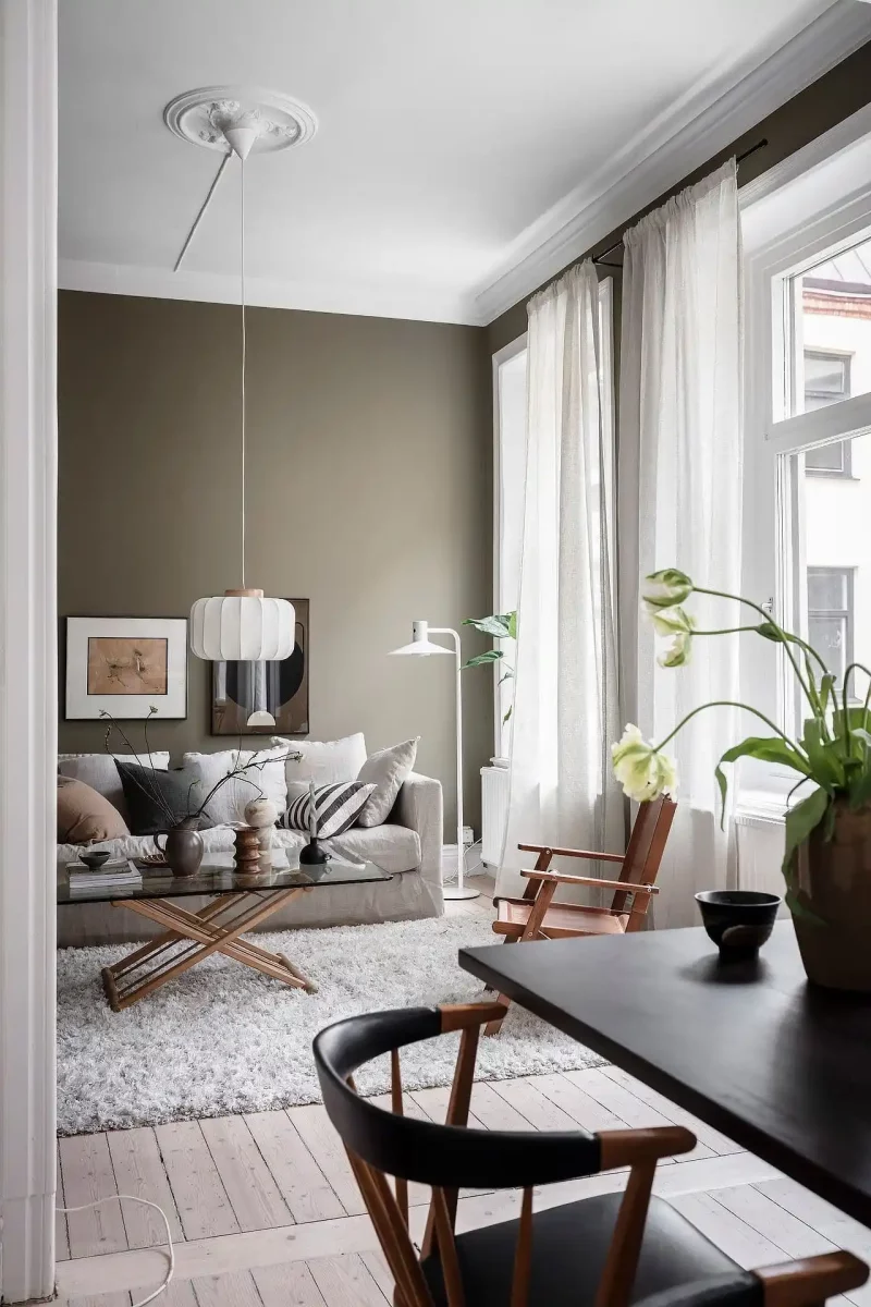 Knusse woonkamer waar olijfgroene muren gecombineerd zijn met zachte aardetinten voor een warme gezellige look.