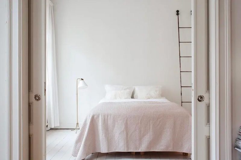 De nude kleur bedsprei komt heel goed naar boven in deze volledige witte slaapkamer. De houten trap naast het bed past er ook perfect bij.