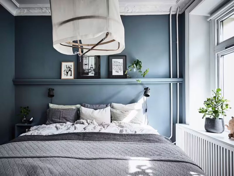 In deze kleine slaapkamer is er gekozen voor een combinatie van petrol kleur muren, een grijs dekbedovertrek set, en en tinten wit en zwart. Ook het groen van het plantje staat er geweldig leuk bij.