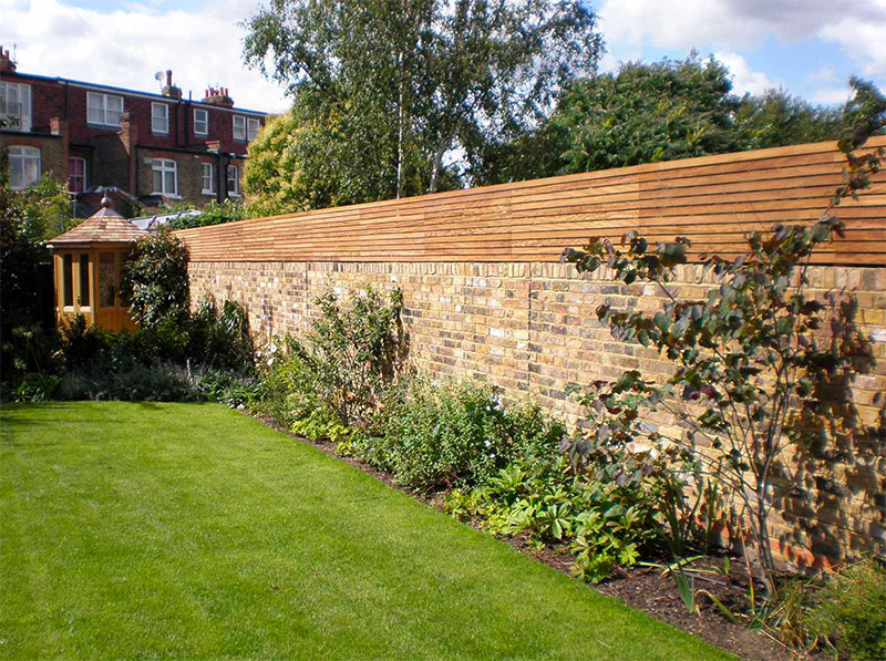 Je kunt een stenen muur in de tuin ook heel mooi combineren met houten schuttingen.