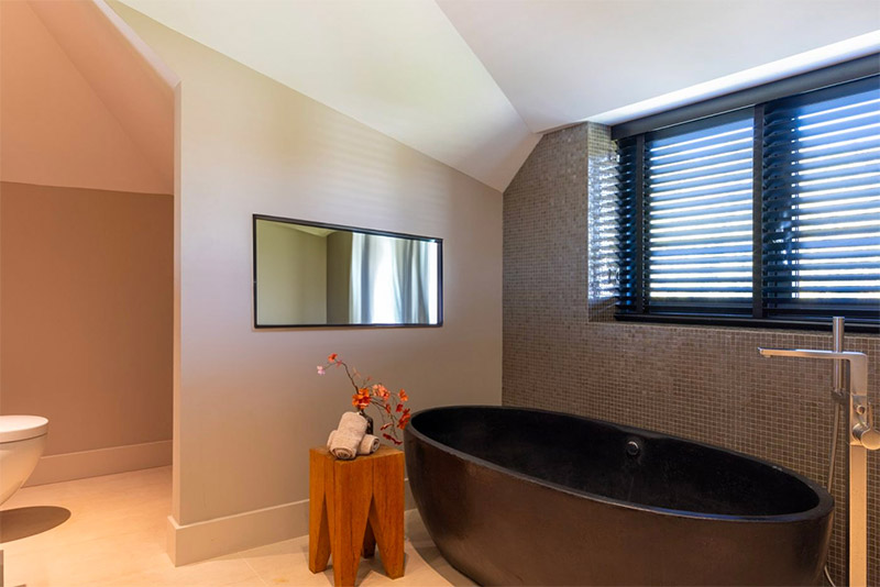 Strakke rechthoekige spiegel boven een luxe ovaal bad.