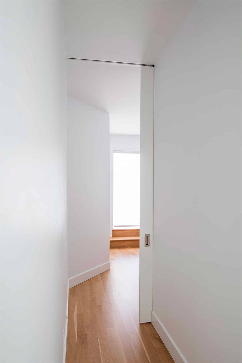 Een strakke plafondhoge witte schuifdeur die in de wand verdwijnt, in een project van MXMA Architecture & Design.