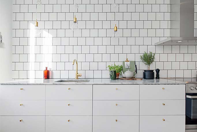 Een mooie witte keuken met een marmer keukenblad en gouden deurknoppen. Klik hier voor meer foto's.