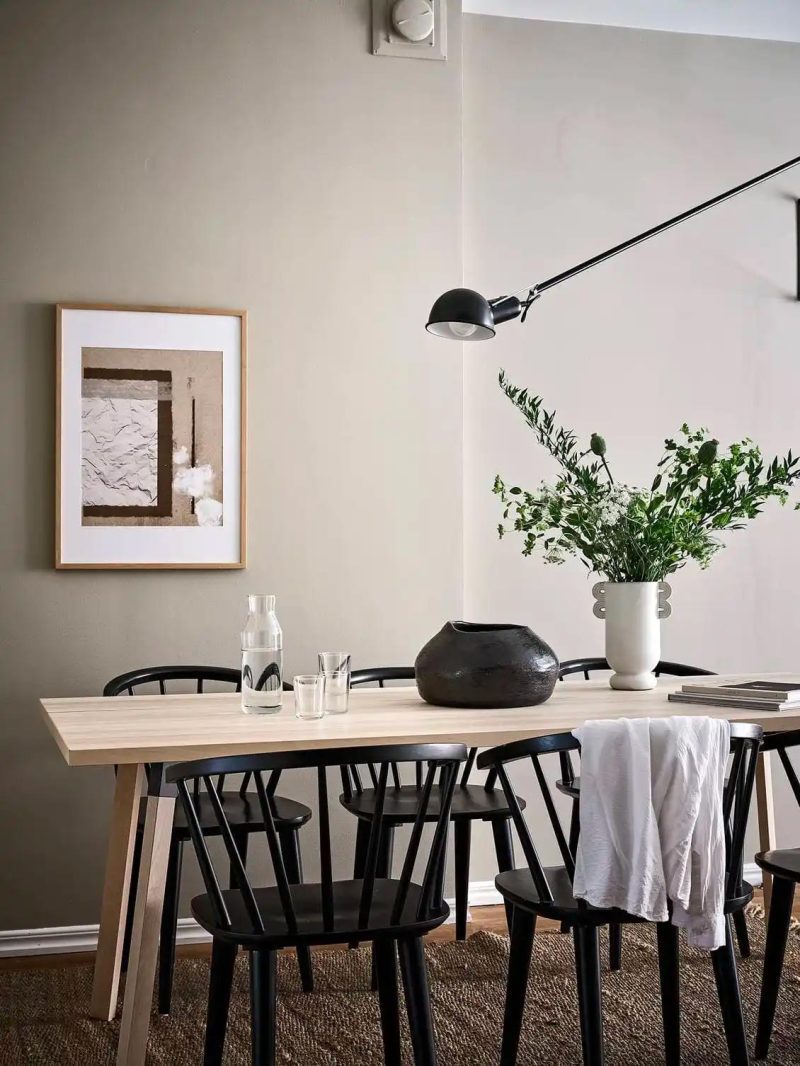 De zandkleur muur staat perfect bij de houten eettafel, zwarte eetkamerstoelen en de zwarte FLOS 265 wandlamp.